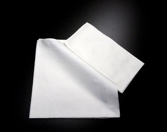 Puede incluir: Dos servilletas de lino blanco, una doblada sobre la otra, sobre un fondo negro.