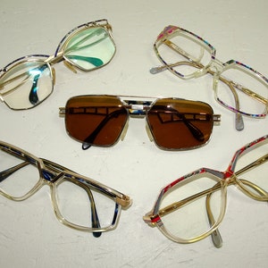 May include: Five pairs of eyeglasses with different colored frames and lenses. The frames are made of metal and plastic and have a variety of geometric shapes. The lenses are clear, tinted, and mirrored.