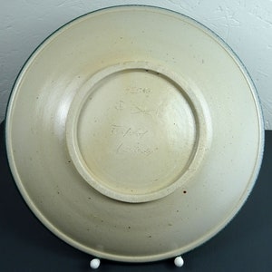 May include: A white ceramic plate with a green rim. The bottom of the plate has a handwritten signature and the number 45638.