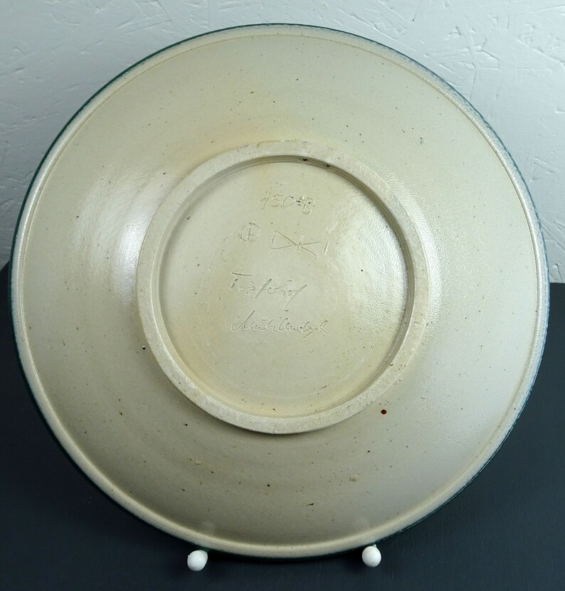 May include: A white ceramic plate with a green rim. The bottom of the plate has a handwritten signature and the number 45638.
