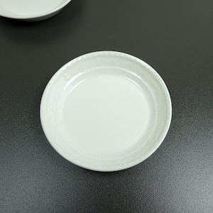 Può includere: Un piattino in ceramica bianca con un bordo decorativo. Il piattino è vuoto e ha una finitura liscia e lucida.