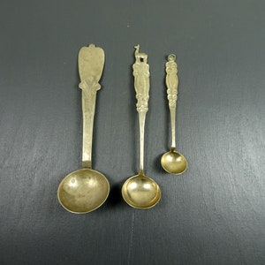 May include: Three silver spoons with ornate handles. The spoons are different sizes and have a rounded bowl shape.