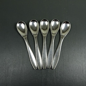 Può includere: Cinque cucchiaini piccoli e lucenti in argento disposti su una superficie grigio scuro. I cucchiaini hanno coppette ovali e manici sottili. Probabilmente per servire o mangiare piccole porzioni.