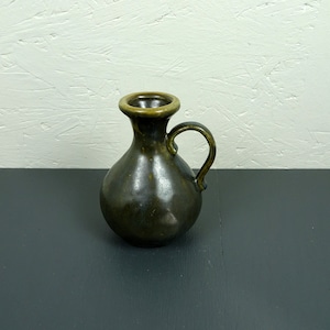 Può includere: Un piccolo vaso in ceramica marrone scuro con un'unica maniglia. Il vaso ha una smaltatura leggermente iridescente.