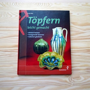 May include: A book titled "Töpfern leicht gemacht" (Pottery Made Easy) with a red and black cover. The cover features ceramic pottery: a green gourd, a white pitcher with blue and green stripes, and a yellow and blue bowl.