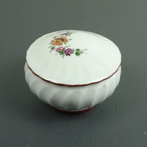 May include: White ceramic trinket box with a floral design and a brown rim. The box has a fluted base and a domed lid.