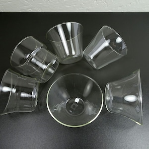 Könnte beinhalten: Sechs durchsichtige Glasbecher in verschiedenen Formen und Größen. Die Becher sind in einem Kreis auf einer schwarzen Oberfläche angeordnet.