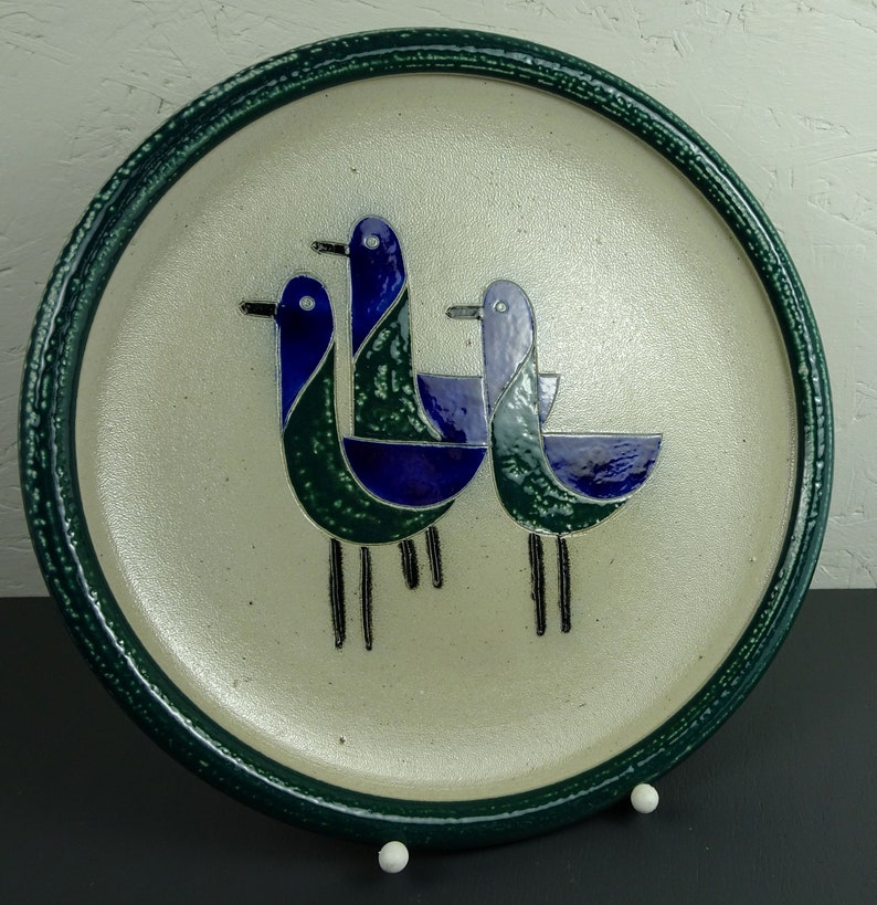 May include: A ceramic plate with a green rim and a white background features a stylized design of three blue and green birds.