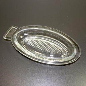May include: A clear glass oval dish with a textured bottom and a handle on one side.