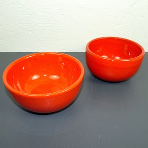Könnte beinhalten: Zwei orangefarbene Keramikschalen in verschiedenen Größen. Die Schalen sind rund und haben eine glatte, glänzende Oberfläche.