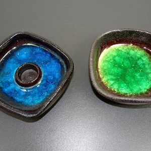 May include: Two square ceramic candle holders with a dark brown glaze. One holder has a teal blue interior with a round hole in the centre. The other holder has a green interior.