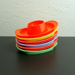 May include: A stack of six colourful plastic egg cups shaped like boats. The cups are stacked in order of colour, starting with orange, then yellow, green, blue, and finally red.