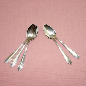 Può includere: Quattro cucchiai d'argento impilati su uno sfondo rosa. I cucchiai sono lucidi e hanno un design semplice.