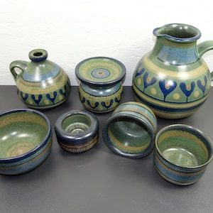 May include: Set of seven green and blue ceramic pottery pieces with a geometric pattern. The set includes a jug, a vase, a bowl, and four small cups.
