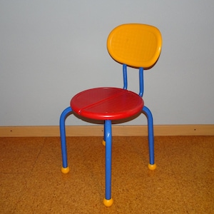May include: A colorful children's chair with a yellow back, red seat, and blue legs. The chair has yellow accents on the legs.