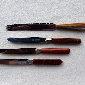 May include: Four different knives with brown, orange, and marbled handles. The knives have silver blades and are arranged vertically on a white surface.