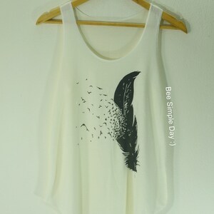 May include: White sleeveless tank top with a black and white graphic print of a feather with birds flying away from it. The text "Bee Simple Day :)" is printed on the right side of the shirt.