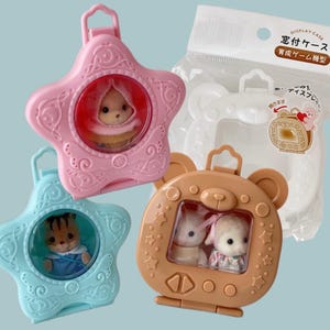 Puede incluir: Una colección de coloridas vitrinas para pequeñas figuras. Las cajas tienen forma de estrella y oso, con ventanas transparentes para exhibir los juguetes. Las cajas son rosas, azules y marrones, con una funda de plástico transparente en el fondo.