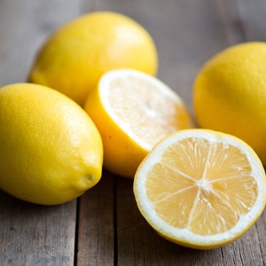 May include: Four lemons on a wooden surface. Three lemons are whole and one is cut in half, revealing the yellow flesh.