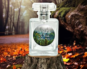 May include: A clear glass bottle of perfume with a silver cap. The label on the bottle says "A Walk In The Woods by Cathleen Nesham". The label has a picture of a forest with trees and a river.