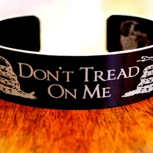 May include: A black metal bracelet with a silver-colored image of a coiled snake and the text "Don't Tread On Me".