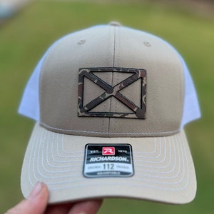 May include: A tan and white trucker hat with a camouflage X logo and a black Richardson 112 label.
