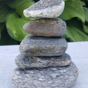May include: A stack of five smooth, gray stones balanced on top of each other. The stones are arranged in a pyramid shape, with the largest stone at the bottom and the smallest stone at the top.