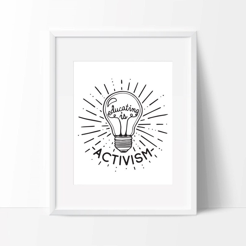 Op de afbeelding: Een zwart-wit print in een lijst met een gloeilampontwerp en de woorden "Educating is Activism". De gloeilamp is omgeven door stralende lijnen en de print zit in een witte lijst.