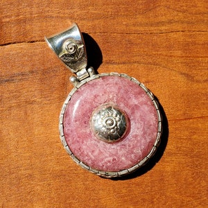 May include: A silver pendant with a pink and white gemstone. The pendant has a detailed design with a floral motif.