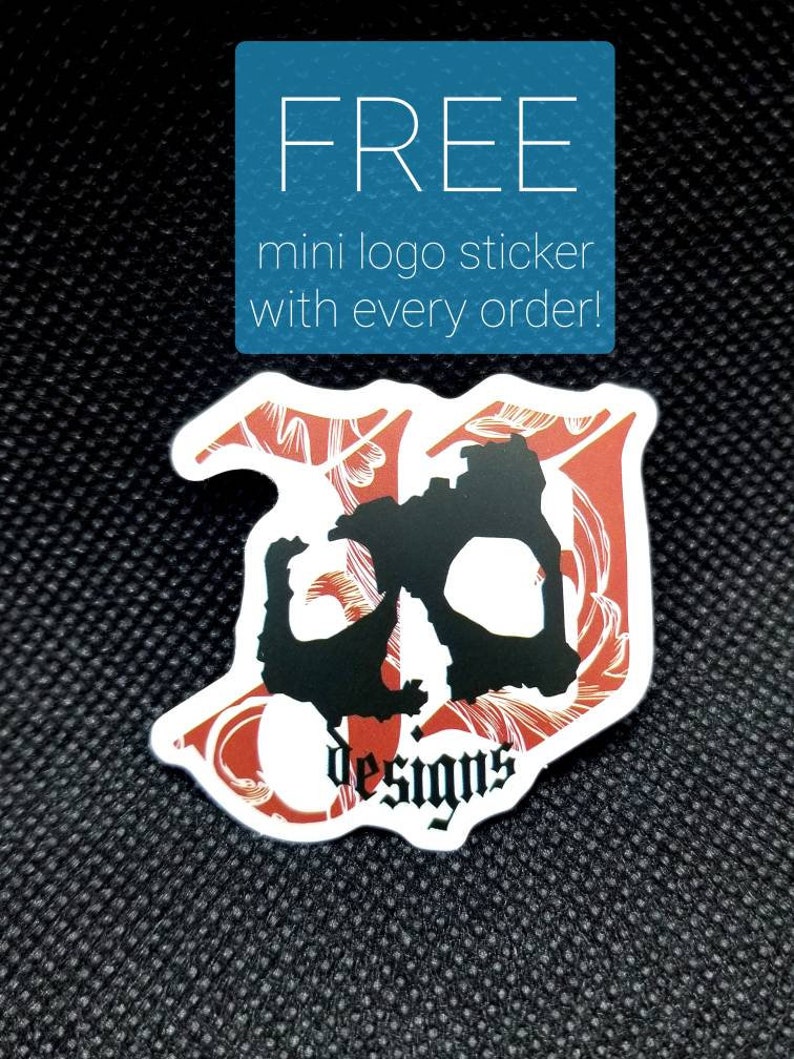 Puede incluir: Una pegatina de calavera roja y negra con el texto "JD Designs" sobre un fondo negro. La pegatina anuncia una pegatina de logotipo mini gratuita con cada pedido.