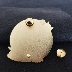 Puede incluir: La parte posterior de un pin de color dorado con un dise&ntilde;o de mariposa. El pin tiene un poste y un cierre de mariposa.