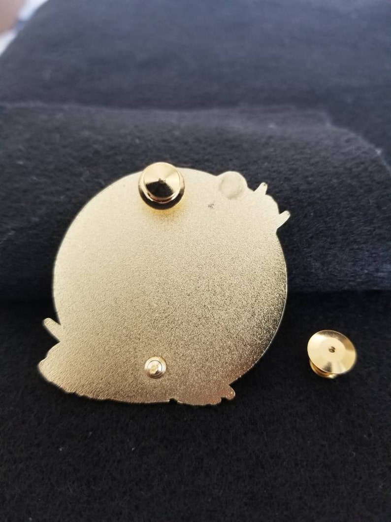 Puede incluir: La parte posterior de un pin de color dorado con un dise&ntilde;o de mariposa. El pin tiene un poste y un cierre de mariposa.