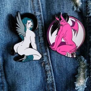 Puede incluir: Dos pines de esmalte que representan a una mujer con alas y una mujer con cuernos y alas. La mujer con alas es blanca con un halo negro y cabello turquesa. La mujer con cuernos es rosa con cabello negro y un halo blanco. Ambos pines est&aacute;n sobre un fondo de mezclilla azul.