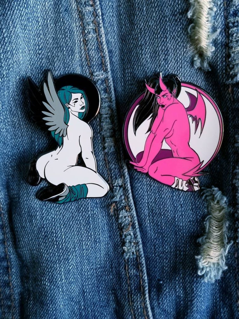 Puede incluir: Dos pines de esmalte que representan a una mujer con alas y una mujer con cuernos y alas. La mujer con alas es blanca con un halo negro y cabello turquesa. La mujer con cuernos es rosa con cabello negro y un halo blanco. Ambos pines est&aacute;n sobre un fondo de mezclilla azul.