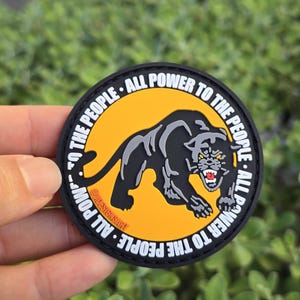 Puede incluir: Parche redondo con un dise&ntilde;o de pantera negra sobre fondo amarillo, rodeado por el texto blanco "ALL POWER TO THE PEOPLE". El parche tiene un borde negro y el texto "@JADESIGNSART".