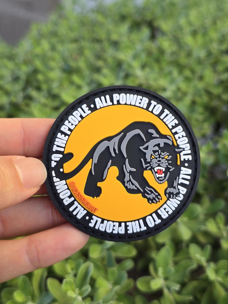 Puede incluir: Parche redondo con un dise&ntilde;o de pantera negra sobre fondo amarillo, rodeado por el texto blanco "ALL POWER TO THE PEOPLE". El parche tiene un borde negro y el texto "@JADESIGNSART".