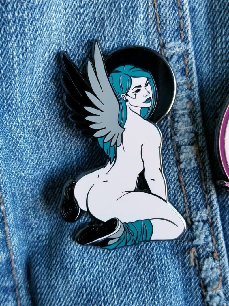 Puede incluir: Un pin de esmalte blanco y negro con un &aacute;ngel arrodillado con alas y cabello turquesa. El &aacute;ngel lleva un halo negro y tiene un cuerpo blanco.