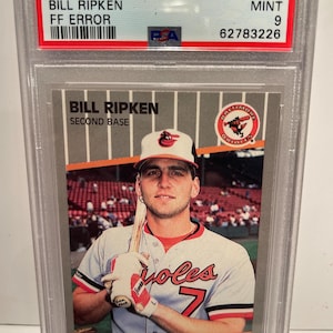 Pode incluir: Um cartão de beisebol Fleer de 1989 com Bill Ripken, classificado como Mint 9. O cartão tem o texto "FF ERROR" e está em um suporte protetor. Mostra Ripken com o uniforme do Baltimore Orioles.