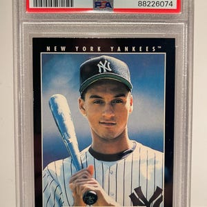 May include: A 1993 Pinnacle Derek Jeter baseball card, graded and encased in a protective holder. The card features a portrait of Jeter in a New York Yankees uniform, holding a bat. The card is graded as Mint 9.