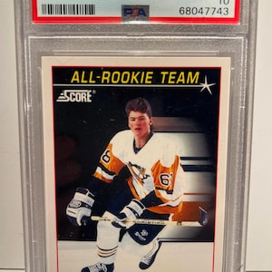 Puede incluir: Una tarjeta de hockey de Jaromir Jagr de 1991 Score American, calificada GEM MT 10 por PSA. La tarjeta presenta a Jagr con su uniforme de los Pittsburgh Penguins, con el texto "ALL-ROOKIE TEAM" y "SCORE". La tarjeta est&aacute; en un soporte protector.