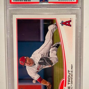 May include: A 2013 Topps Mike Trout baseball card, graded GEM MT 10 by PSA, featuring a player in a white and red uniform. The card is encased in a protective holder.