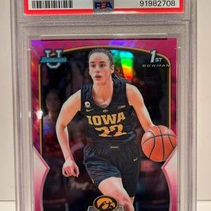 May include: A Caitlin Clark pink refractor trading card from the 2022 Bowman University set. The card features a photo of Clark in her Iowa Hawkeyes basketball uniform, dribbling a basketball. The card is graded GEM MT 10.