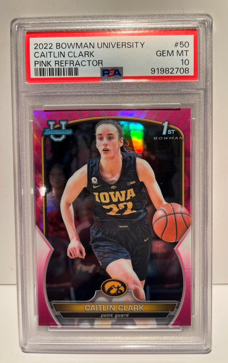 May include: A Caitlin Clark pink refractor trading card from the 2022 Bowman University set. The card features a photo of Clark in her Iowa Hawkeyes basketball uniform, dribbling a basketball. The card is graded GEM MT 10.
