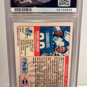 May include: A graded Barry Sanders football card from the 1989 Pro Set NFL series. The card features a photo of Sanders in a Detroit Lions uniform, with biographical information and statistics. The card is encased in a protective holder.