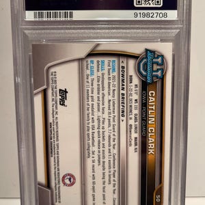 May include: A Caitlin Clark Bowman trading card, encased in a protective holder. The card features a photo of Caitlin Clark, an Iowa point guard. The card's details include her height, weight, and college information. The card is graded by PSA.