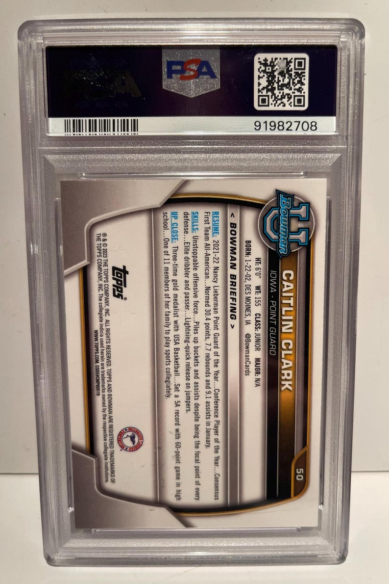 May include: A Caitlin Clark Bowman trading card, encased in a protective holder. The card features a photo of Caitlin Clark, an Iowa point guard. The card's details include her height, weight, and college information. The card is graded by PSA.