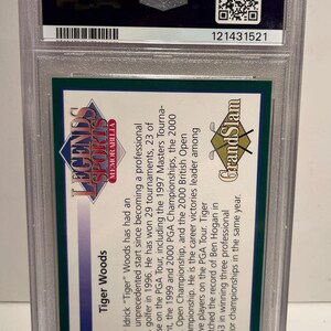 Puede incluir: Una tarjeta coleccionable de Tiger Woods Legends Sports Memorabilia, encapsulada en un soporte protector de pl&aacute;stico. La tarjeta presenta texto sobre la carrera de Woods, incluyendo victorias en torneos. El logo de PSA es visible.