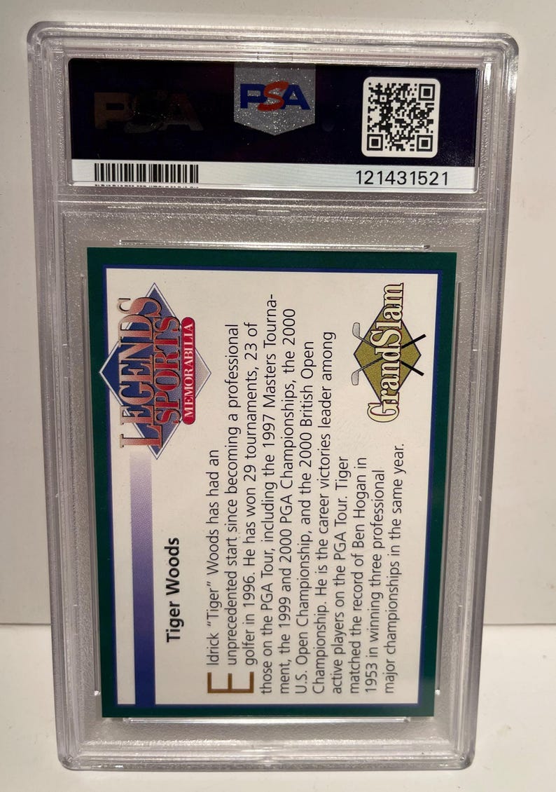 Puede incluir: Una tarjeta coleccionable de Tiger Woods Legends Sports Memorabilia, encapsulada en un soporte protector de pl&aacute;stico. La tarjeta presenta texto sobre la carrera de Woods, incluyendo victorias en torneos. El logo de PSA es visible.