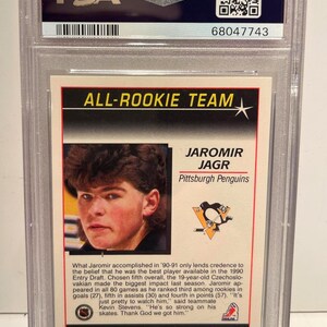 Puede incluir: Una tarjeta de hockey de Jaromir Jagr de los Pittsburgh Penguins, calificada y encapsulada por PSA. La tarjeta es del conjunto All-Rookie Team de 1991 de Score, con la imagen de Jagr y el logotipo del equipo.