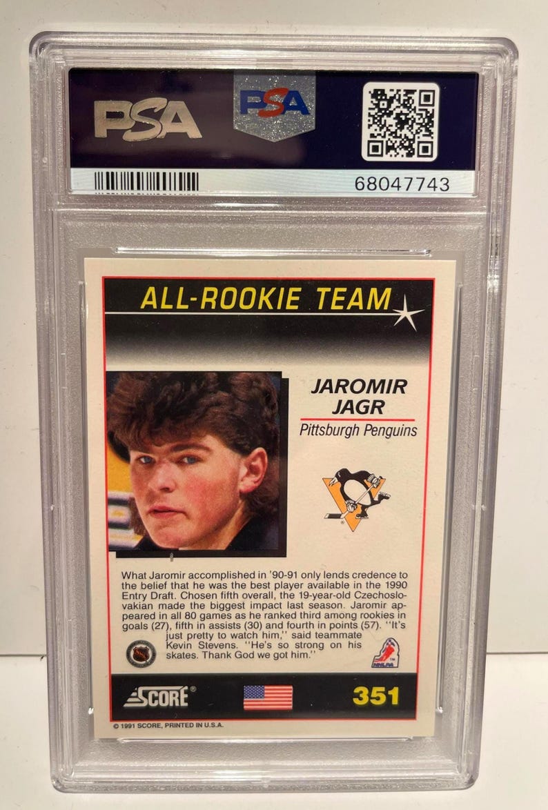 Puede incluir: Una tarjeta de hockey de Jaromir Jagr de los Pittsburgh Penguins, calificada y encapsulada por PSA. La tarjeta es del conjunto All-Rookie Team de 1991 de Score, con la imagen de Jagr y el logotipo del equipo.